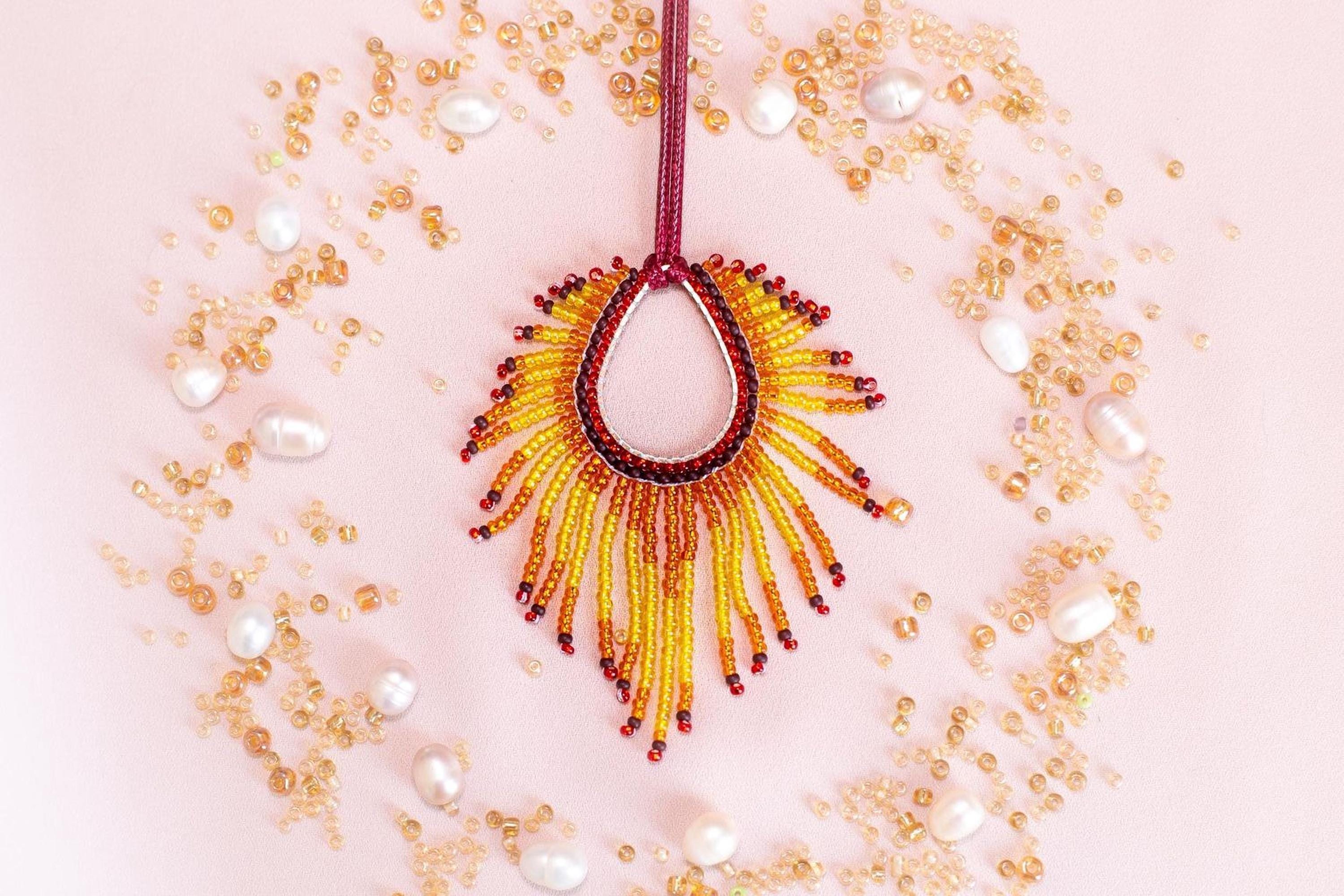 a vibrant, beaded necklace with a large, sun-like pendant surrounded by an array of small, round, and round beads in various colors, including gold, white, and red.